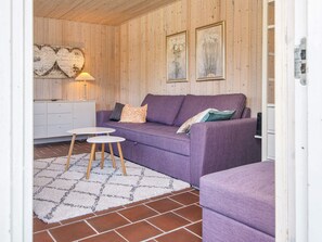 A cozy room with a purple sofa, a small white table, and a patterned rug. - Holiday Home in Glesborg (Glesborg)