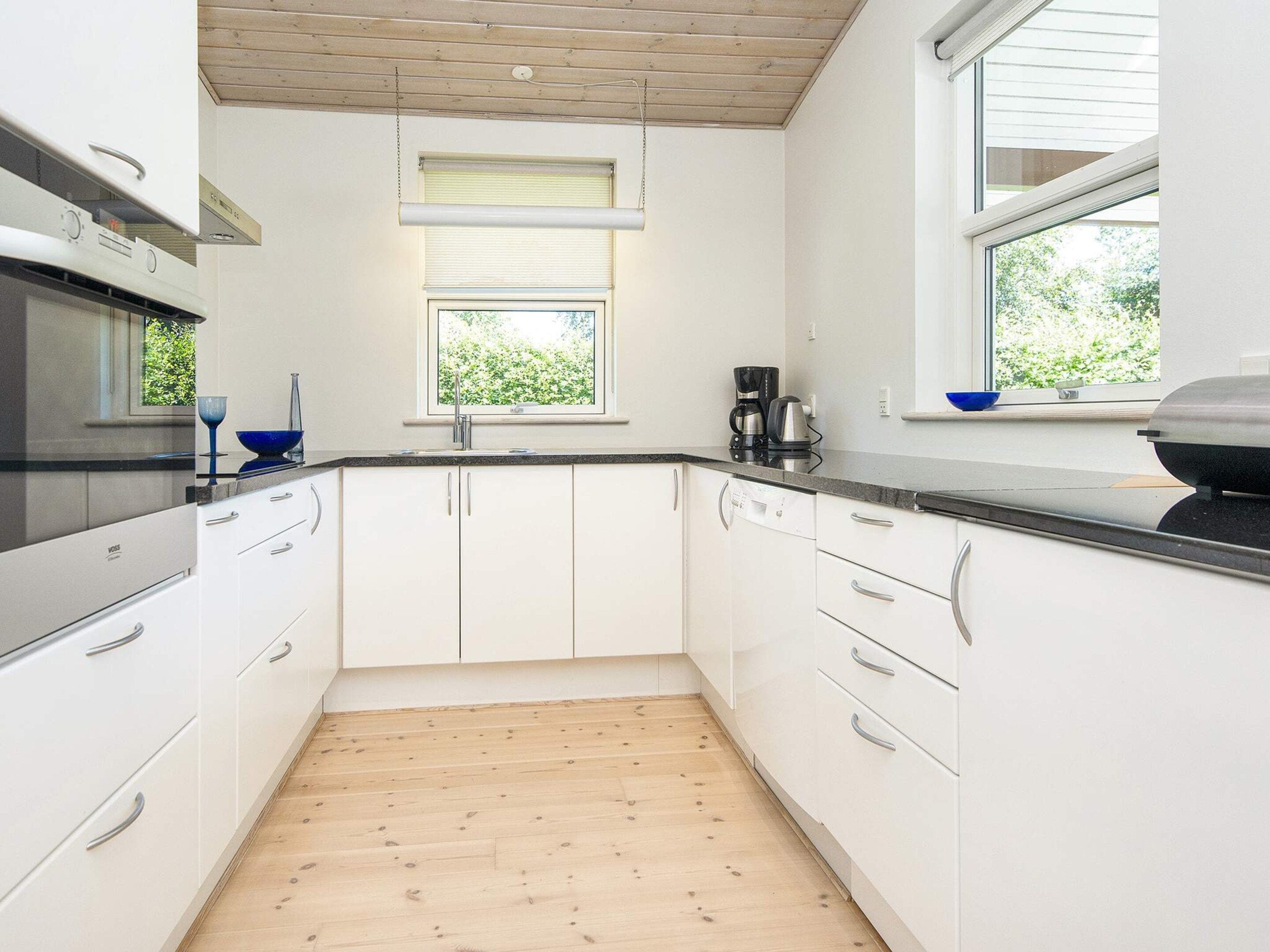 A modern kitchen with white cabinets, a wooden floor, and a window with blinds.