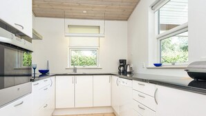 Eine moderne Küche mit weißen Schränken, Holzboden und einem Fenster mit Jalousien.