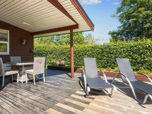 A wooden deck with outdoor furniture, including a table and chairs, and a covered area with a roof. - Holiday Home in Glesborg (Glesborg)