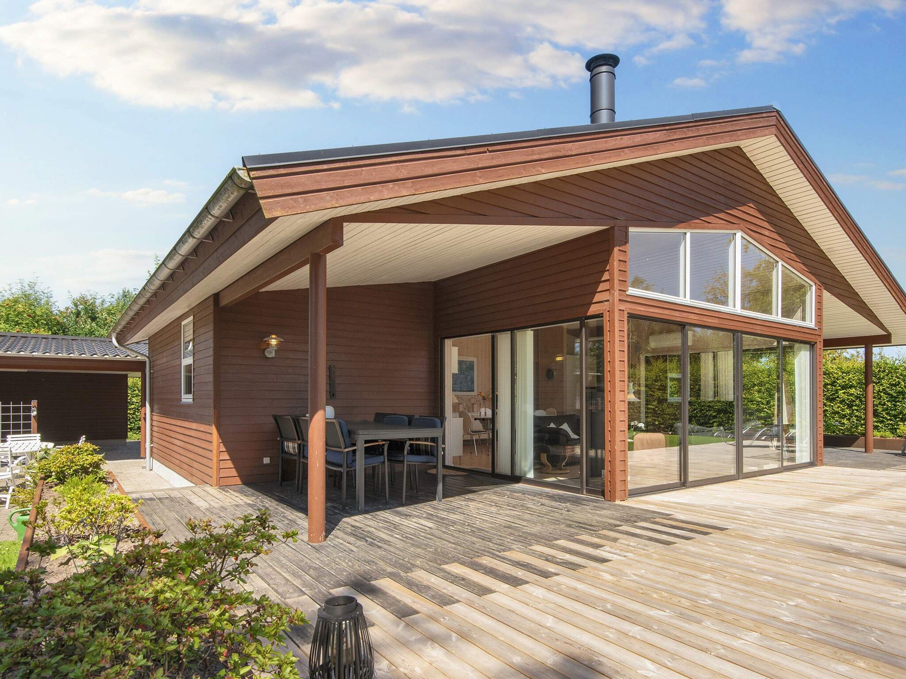 A modern house with a covered patio area, a chimney, and a large glass door leading to an interior space.