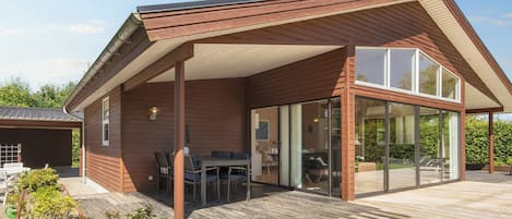 A modern house with a covered patio area, a chimney, and a large glass door leading to an interior space.