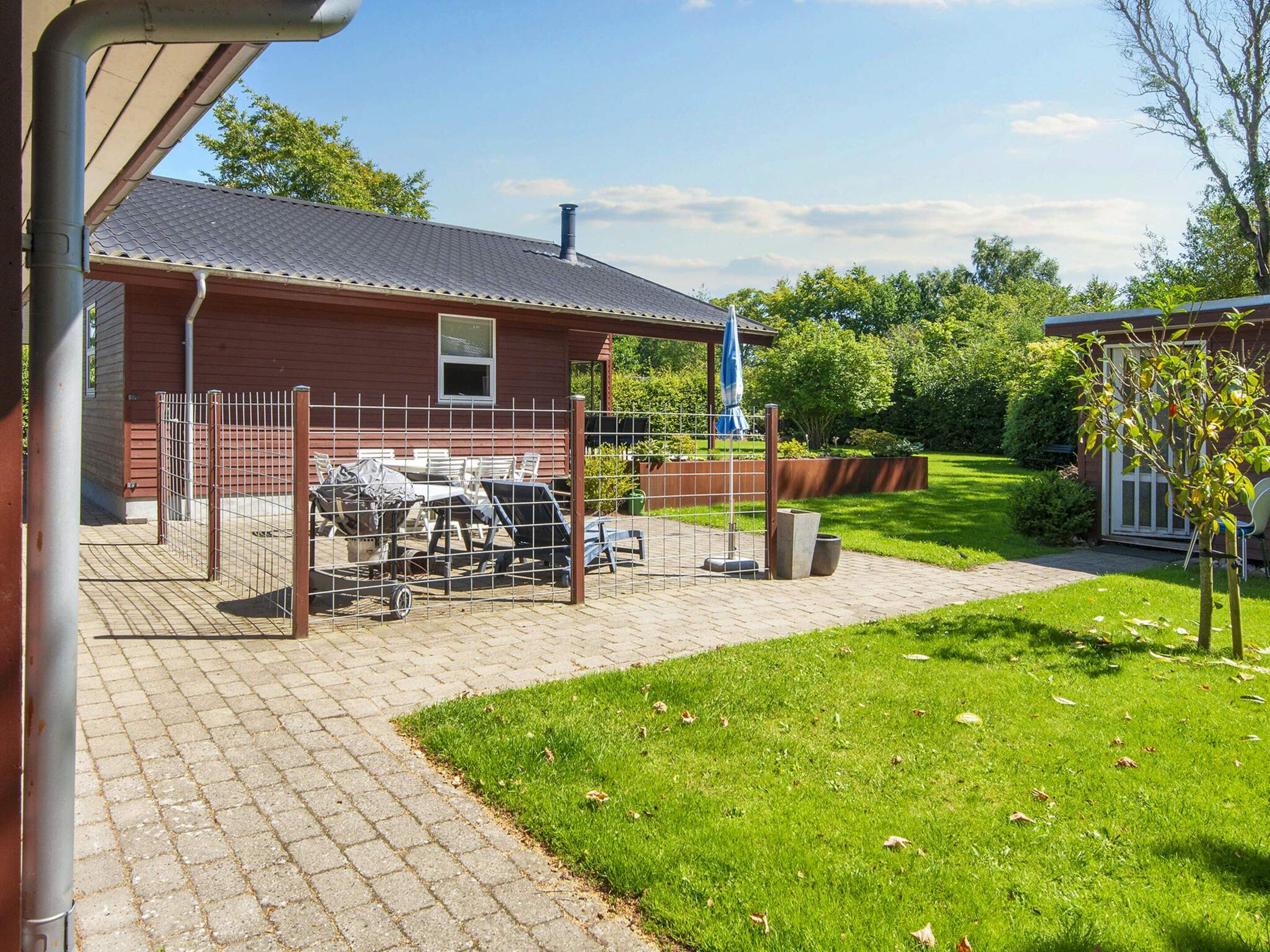 Een overdekt terras met een patio, een tafel met stoelen en een omheinde tuin.