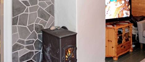 A stone wall, a wood-burning stove, and a television in a living room.