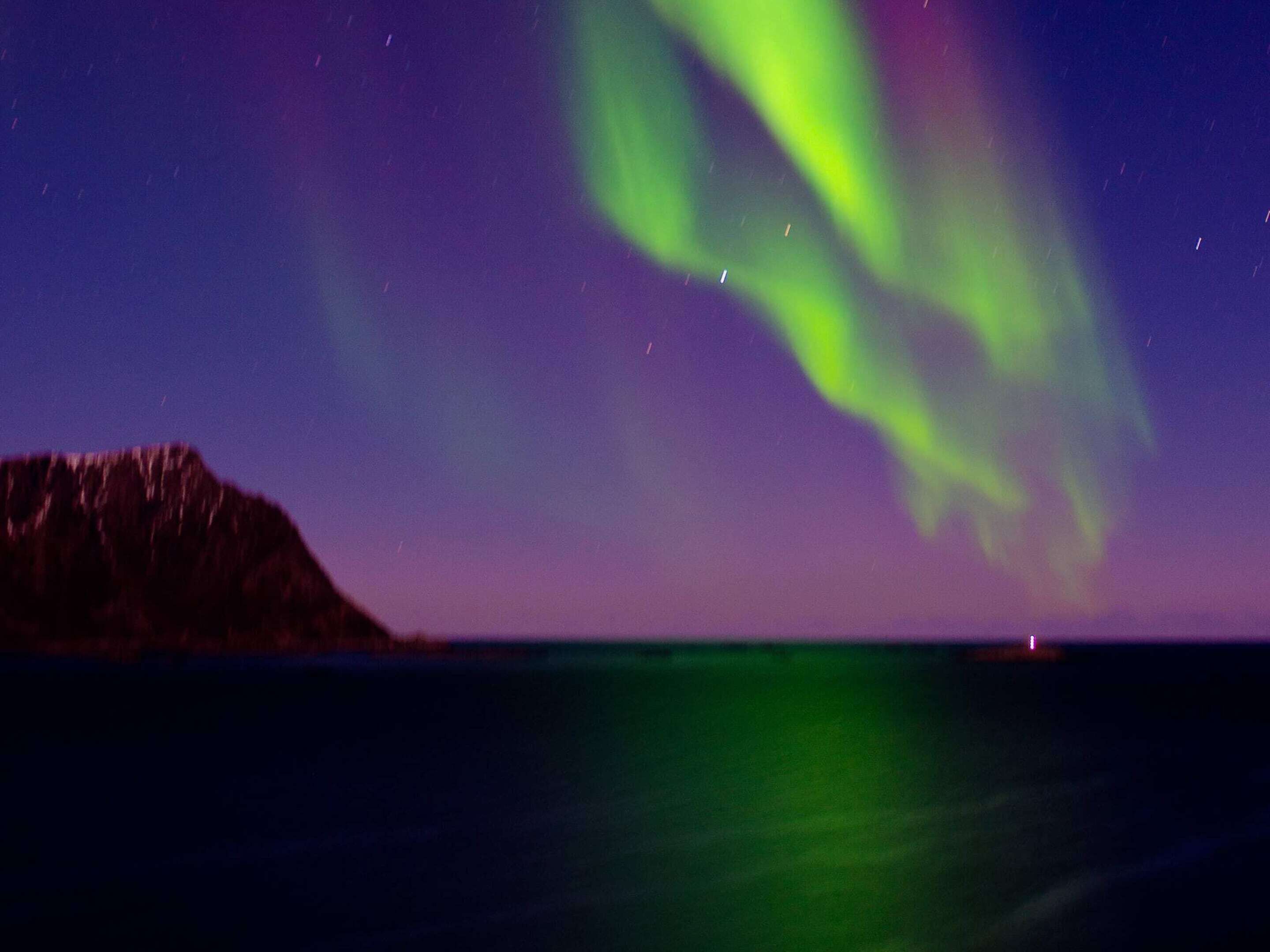 Una vista nocturna de las auroras boreales sobre un cuerpo de agua, con una montaña en primer plano.