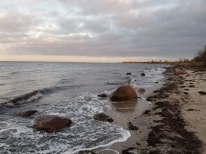 A beach with waves, rocks, and a cloudy sky.