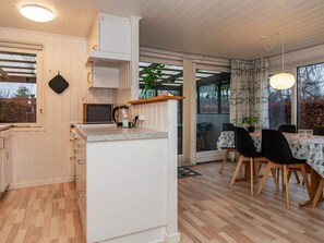 Eine moderne Küche mit Einbauherd, ein Essbereich mit Tisch und Stühlen sowie ein großes Fenster mit Blick ins Freie.
