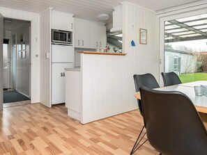 A compact kitchen with white cabinets, a microwave, and a refrigerator. There is a dining area with a table and chairs, and a view of the outdoors through a glass door.