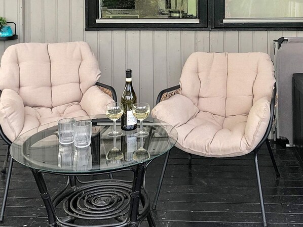Two cushioned chairs facing each other around a glass table with a bottle and glasses on it.