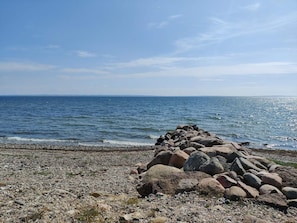 A rocky shoreline with a pile of large rocks in the foreground and calm sea under a clear sky.
