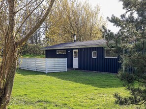 A small, single-story building with a white door and windows, surrounded by a white fence and trees. - 5 Person Holiday Home in Hurup Thy (Hurup Thy)