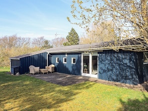 A blue building with a covered patio, a small garden, and a view of the surrounding trees.