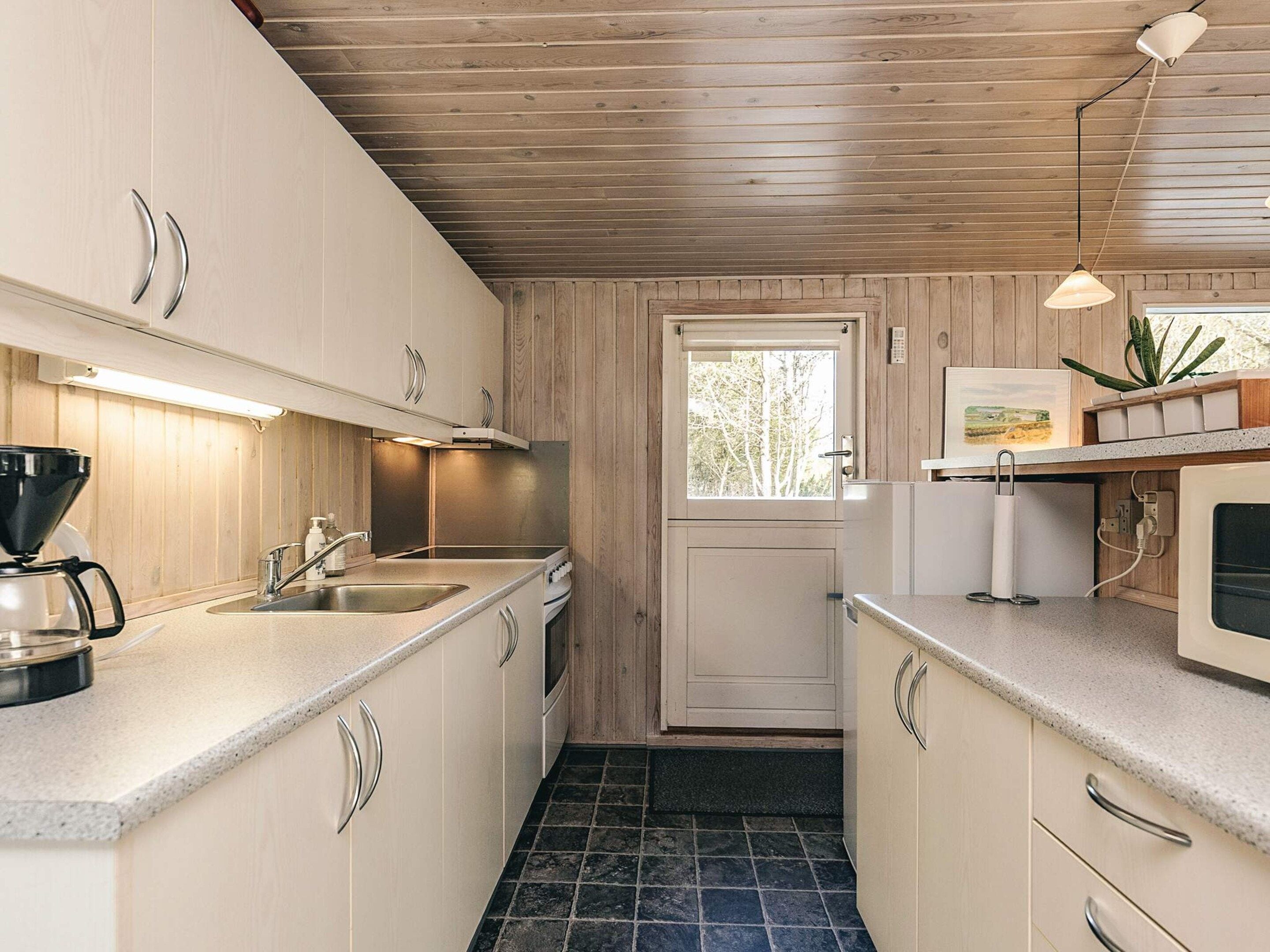 A compact kitchen with wooden cabinets, a sink, a coffee maker, and a microwave.