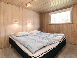 Una habitación con cama, paredes de madera, una ventana y luces fijadas a la pared.