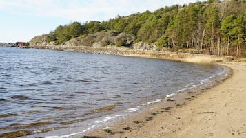 A sandy beach with gentle waves, a rocky shoreline, and a forested area in the background.