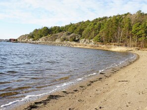 A sandy beach with gentle waves, a rocky shoreline, and a forested area in the background. - 4 Star Holiday Home in Stromstad (Stromstad)