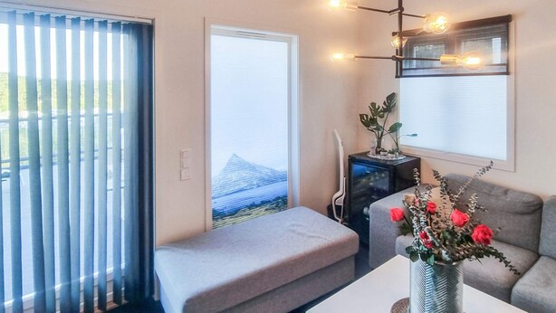 A modern living room with a grey sofa, a small bench, a white table with a vase of flowers, and a black cabinet. - 4 Star Holiday Home in Stromstad (Stromstad)
