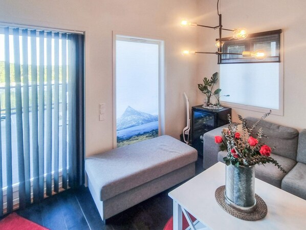 Uma sala de estar moderna com um sofá cinzento, um pequeno banco, uma mesa branca com um vaso de flores e um armário preto.