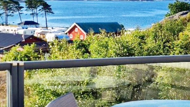 A balcony with a round table and a chair, overlooking a coastal area with houses and a clear view of the sea. - 4 Star Holiday Home in Stromstad (Stromstad)