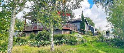 A modern house with a wooden deck and a large window overlooking a lush garden.