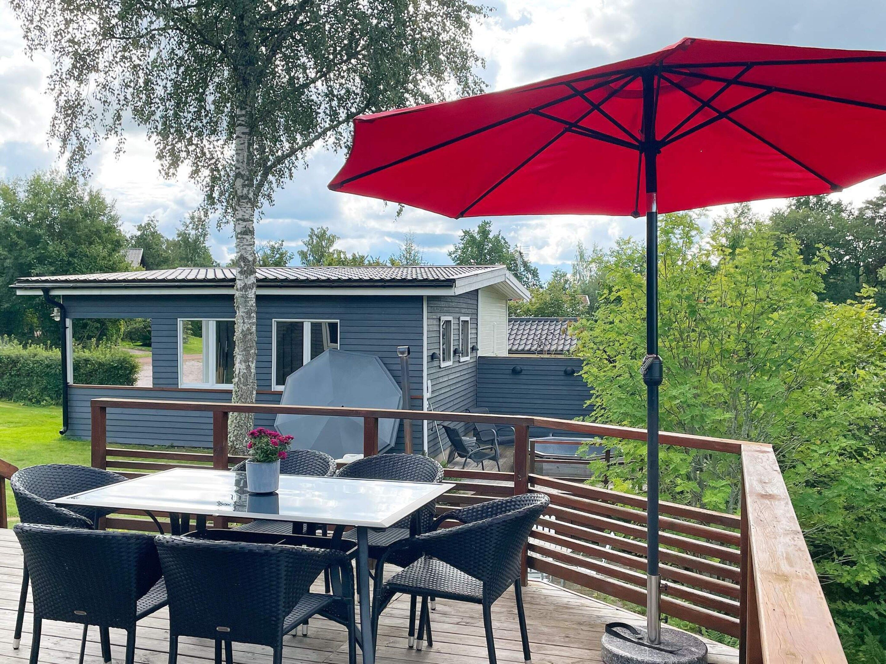 Una terraza con mesa y sillas, una parrilla de barbacoa y un paraguas rojo.