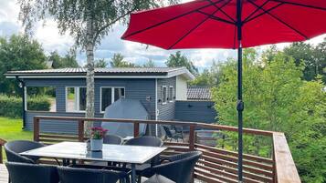 A deck with a table and chairs, a barbecue grill, and a red umbrella.