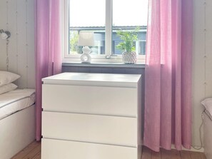 A bedroom with a white dresser, a bedside table with a lamp, and a window with pink curtains. - 6 Person Holiday Home in Granna (Gränna)