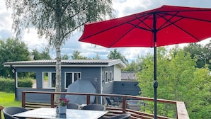 Una terraza con una mesa, sillas, una parrilla y un paraguas rojo.