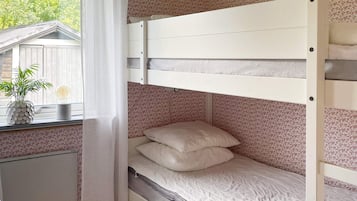 A bunk bed with a mattress and pillows, a window with a curtain, and a plant on the windowsill.