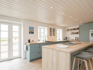 A modern kitchen with a large island, built-in appliances, and a view through the glass doors. - Holiday Home in NykÃ¸bing M (Nykobing Mors)