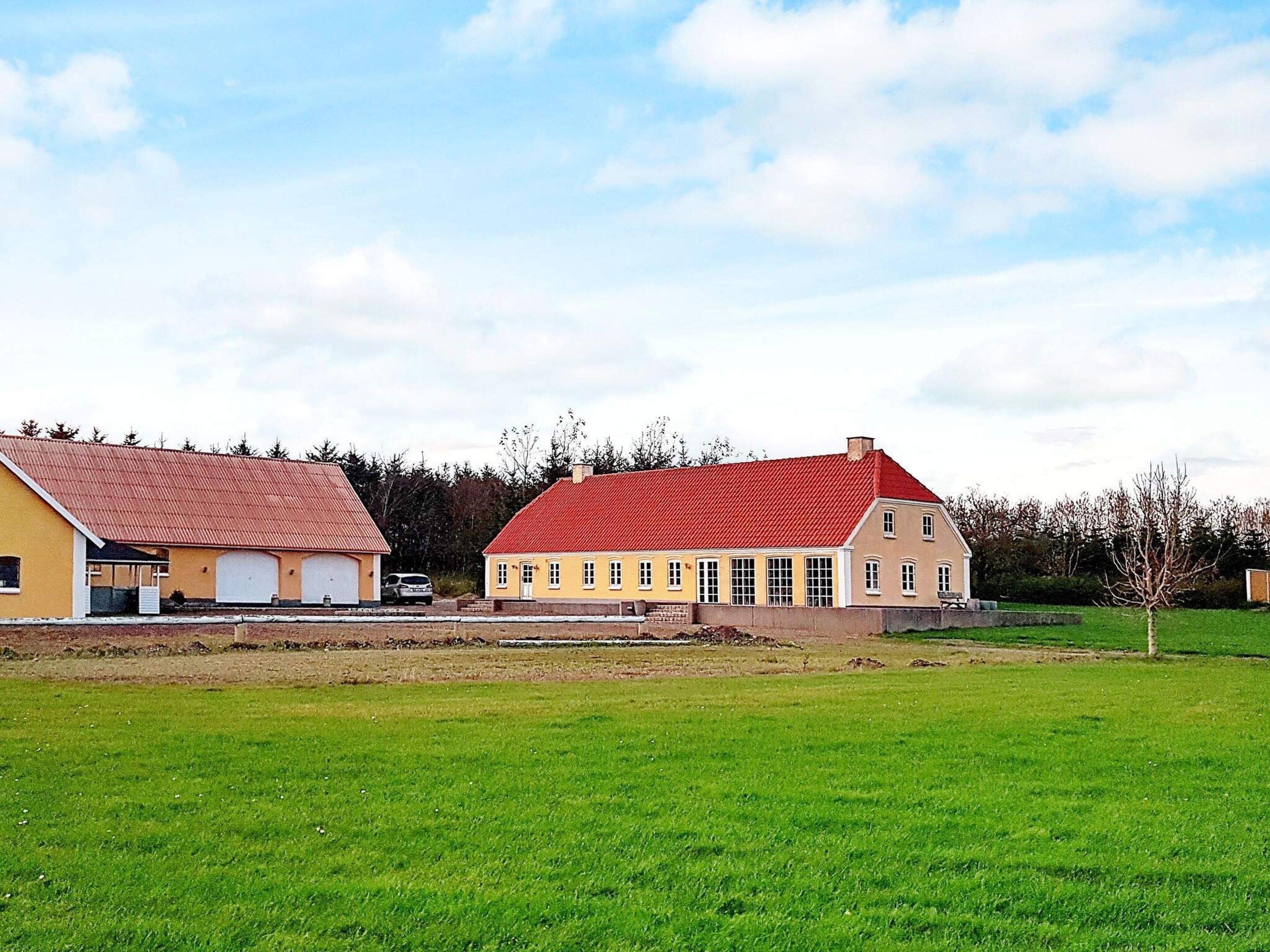 A two-story building with a red roof and yellow walls, adjacent to a green field.