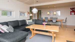 A modern living room with a sectional sofa, a wooden dining table, and a kitchen area in the background. - 6 Person Holiday Home in Knebel (Knebel)
