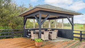 A covered outdoor seating area with a table and chairs, a grill, and a potted plant. - 6 Person Holiday Home in Knebel (Knebel)