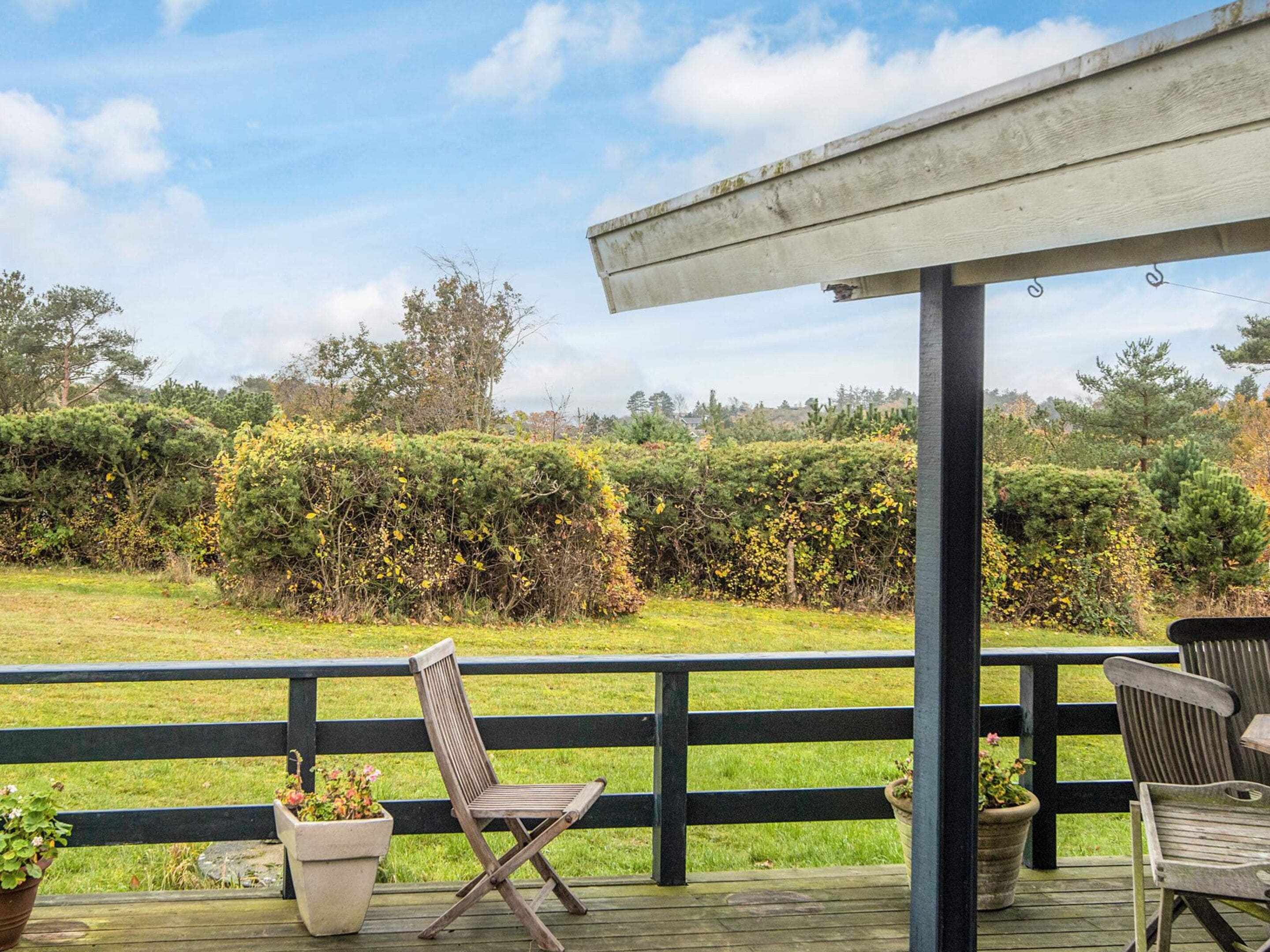A wooden deck with two chairs and a table, overlooking a grassy area with dense shrubbery and trees.