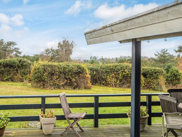 A wooden deck with two chairs and a table, overlooking a grassy area with dense shrubbery and trees.