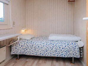 A single bed with a floral bedspread, a bedside table, and a wall-mounted light fixture.
