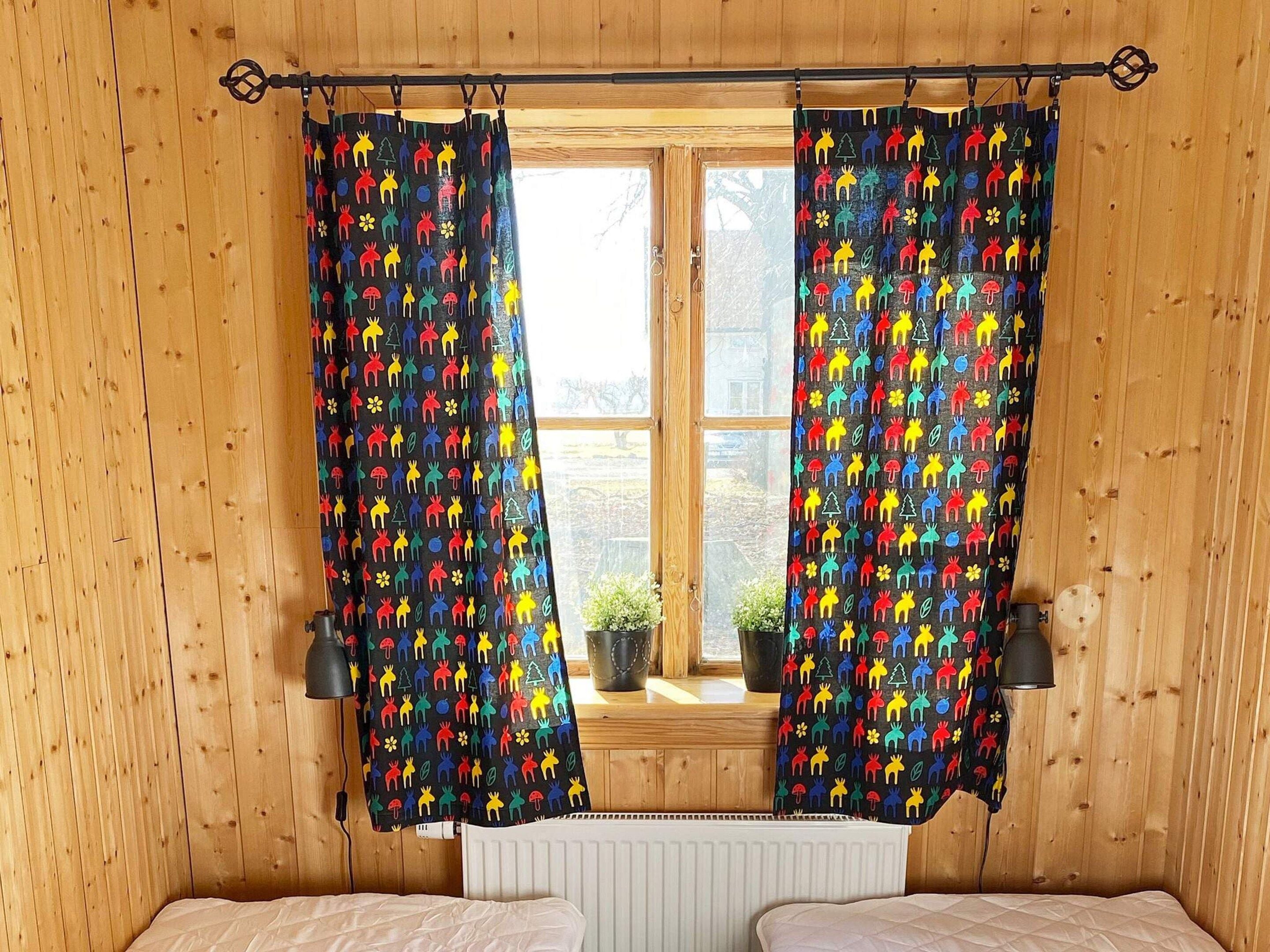 A room with wooden walls, a window with curtains, a radiator, and two bedside tables.