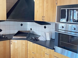 A modern kitchen with wooden cabinets, a black countertop, and stainless steel appliances including an oven and a microwave. - 8 Person Holiday Home in Granna (Gränna)