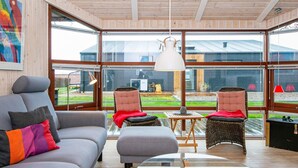 A modern living room with a grey sofa, two wicker chairs, a glass coffee table, and large windows offering a view of the backyard.