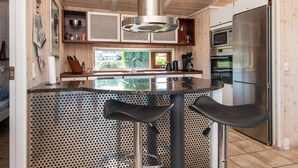A modern kitchen with a central island, stainless steel appliances, and a view of greenery outside.