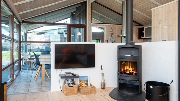 A modern living room with a large TV, a wood-burning stove, wicker baskets, and a dining area with a table and chairs.