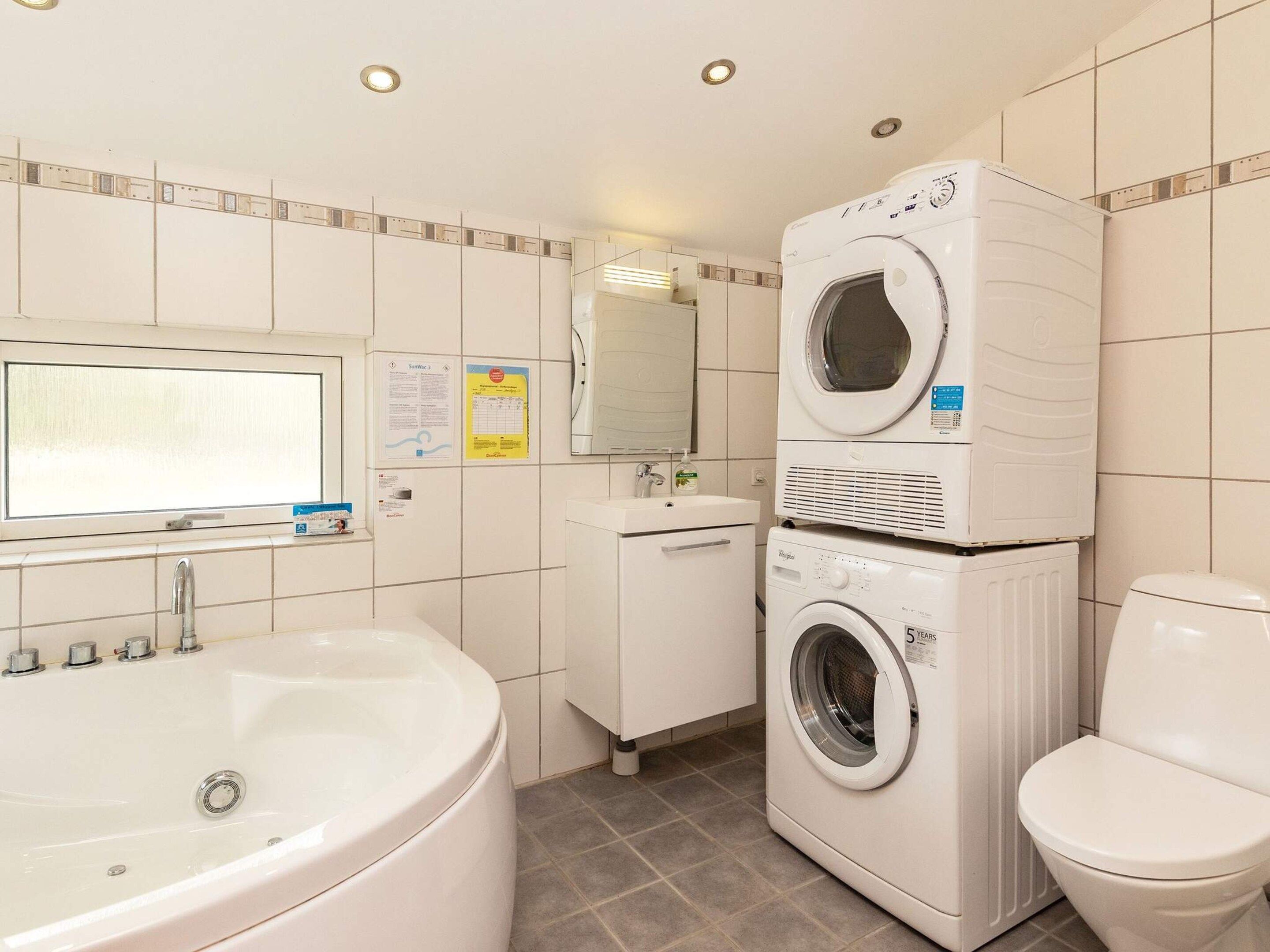 A bathroom with a bathtub, a stacked washer and dryer, a toilet, and a mirror.
