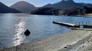 Un lac paisible, avec une jetée qui s’avance sur l’eau, entouré de montagnes et surplombé d’un ciel dégagé.