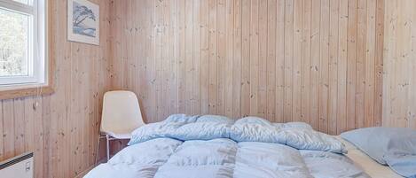 A bedroom with a bed, a chair, and wooden walls.