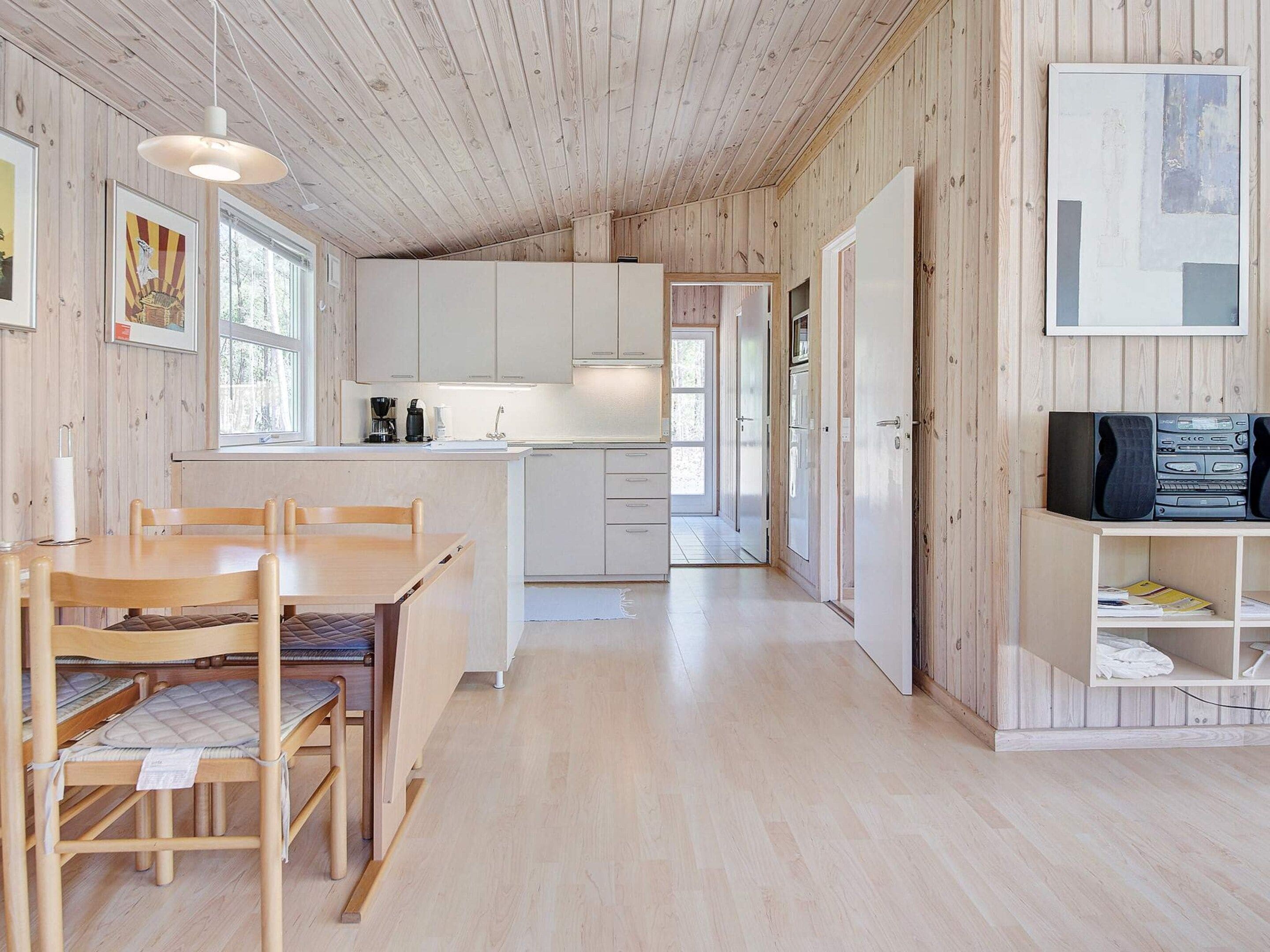 Una cocina moderna con armarios blancos, un comedor con mesa y sillas de madera, y un televisor en un estante.