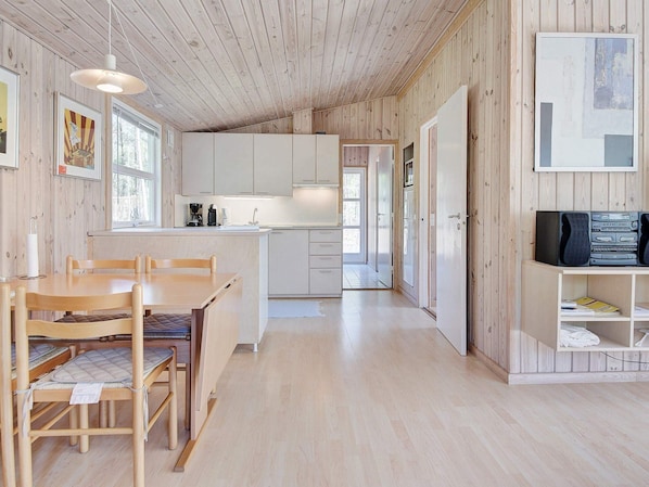 Een modern cabin interieur met houten details, een eethoek met tafel en stoelen, een keuken met witte kastjes en een televisie op een plank.