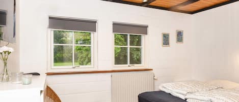 A bedroom with a bed, two windows, a radiator, a wooden ceiling, and a wall-mounted light fixture.
