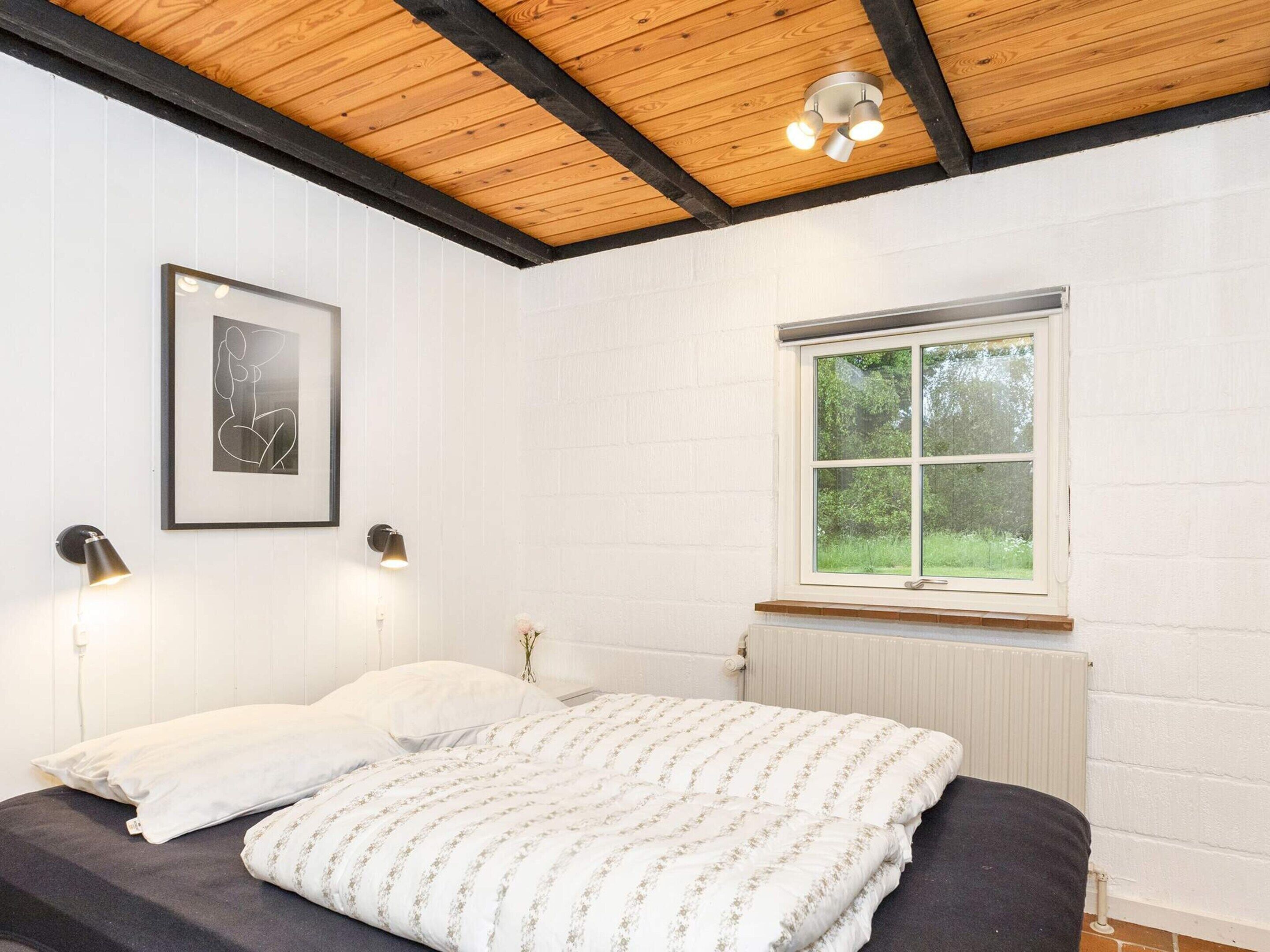Een slaapkamer met een bed, een raam, een radiator en een ingelijst schilderij aan de muur.