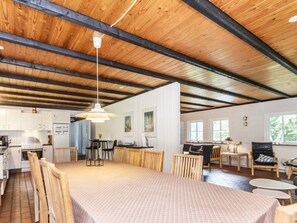 A spacious dining area with a long table and chairs, a kitchen in the background, and a wooden ceiling. - 6 Person Holiday Home in Bindslev (Bindslev)