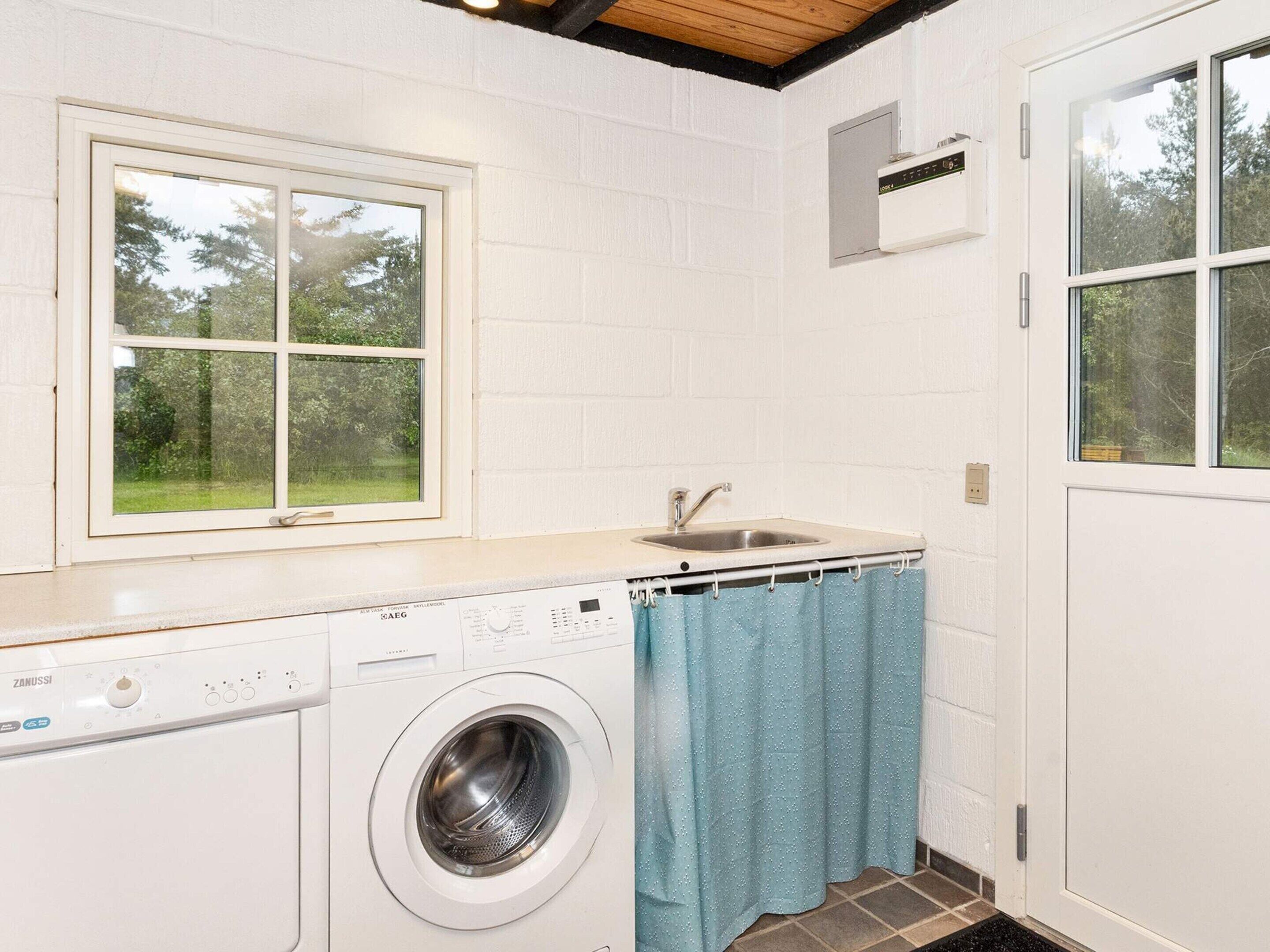 A laundry room with a washing machine, a sink, and a window.